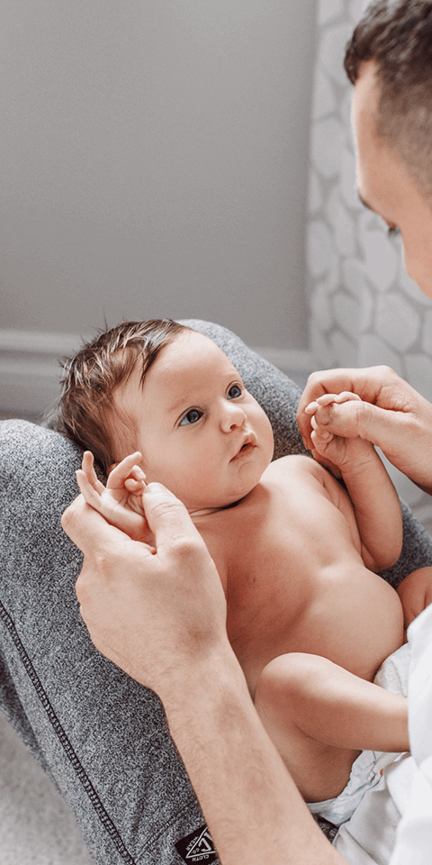 Gateshead Fertility: A father sitting on the floor of his home with a newborn baby lying on his legs as he looks into its eyes.